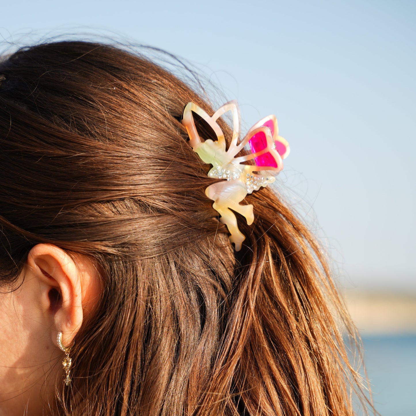 Close-up of a person's hair with a colorful butterfly clip against a blurred natural background