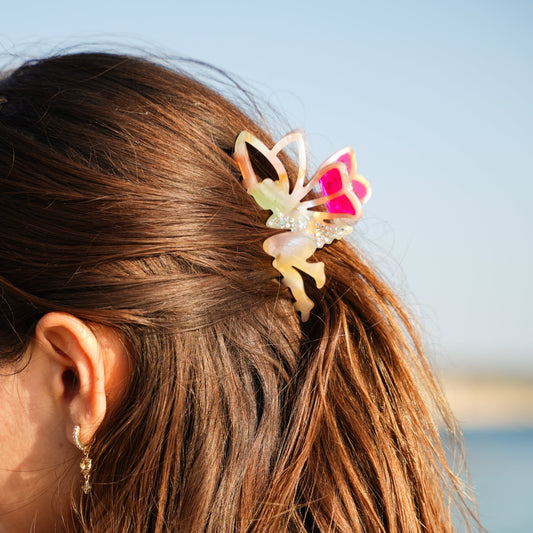 Close-up of a person's hair with a colorful butterfly clip against a blurred natural background